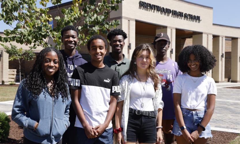 Seven students standing in front of a school